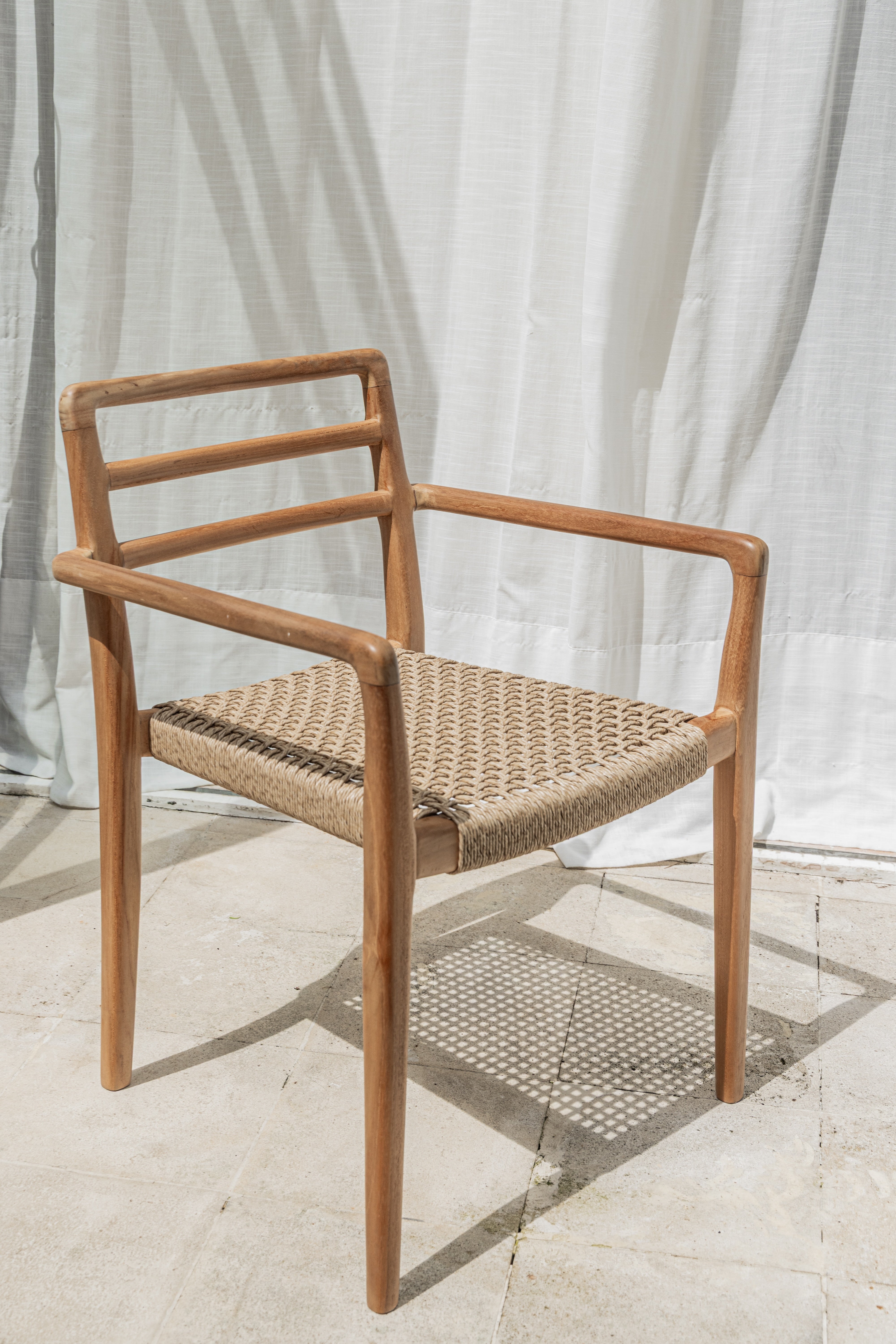 Lila teak dining chair with woven wicker seat on a sunny patio