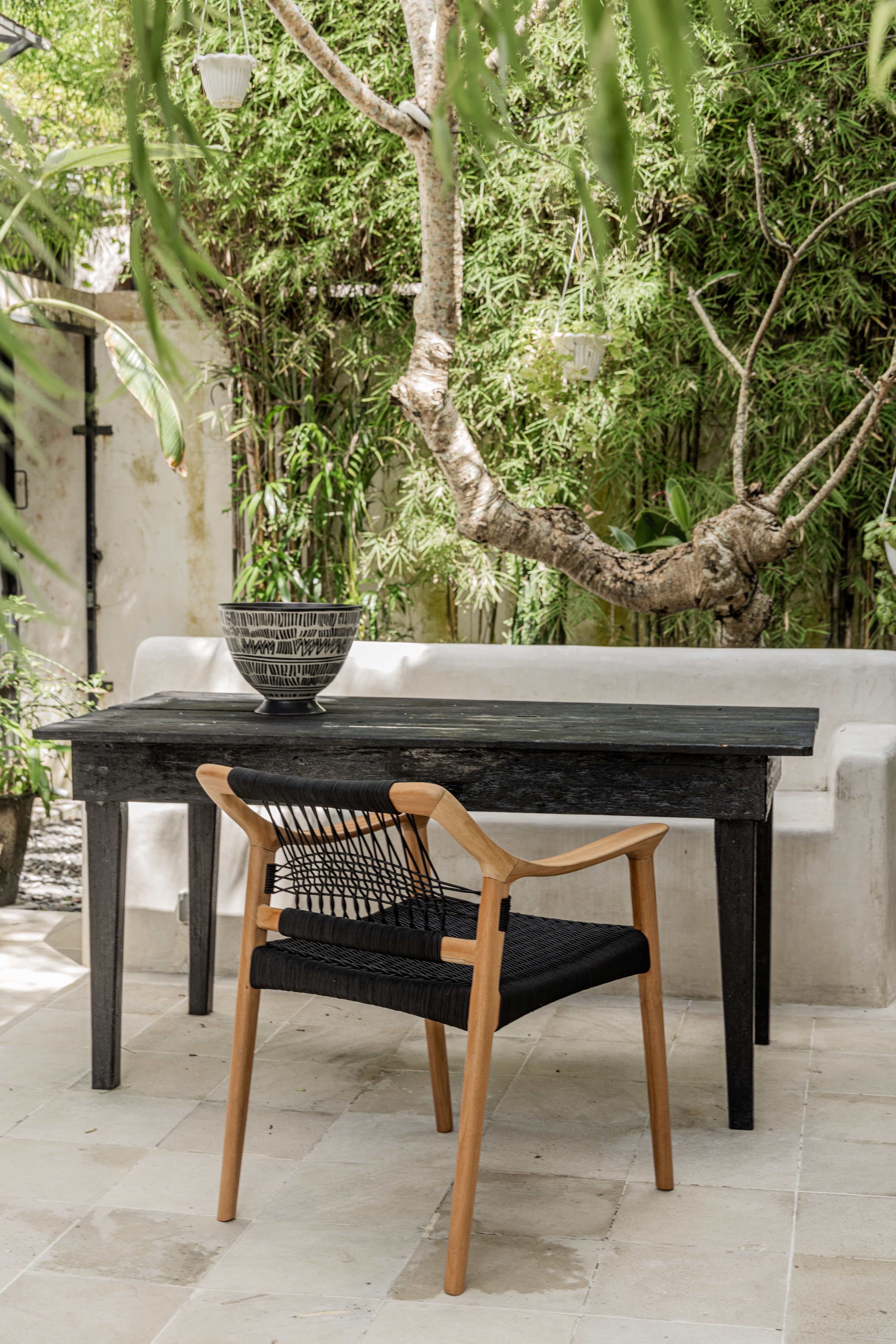 Norwegian inspired teak dining chair with black woven rope seat and back in outdoor setting