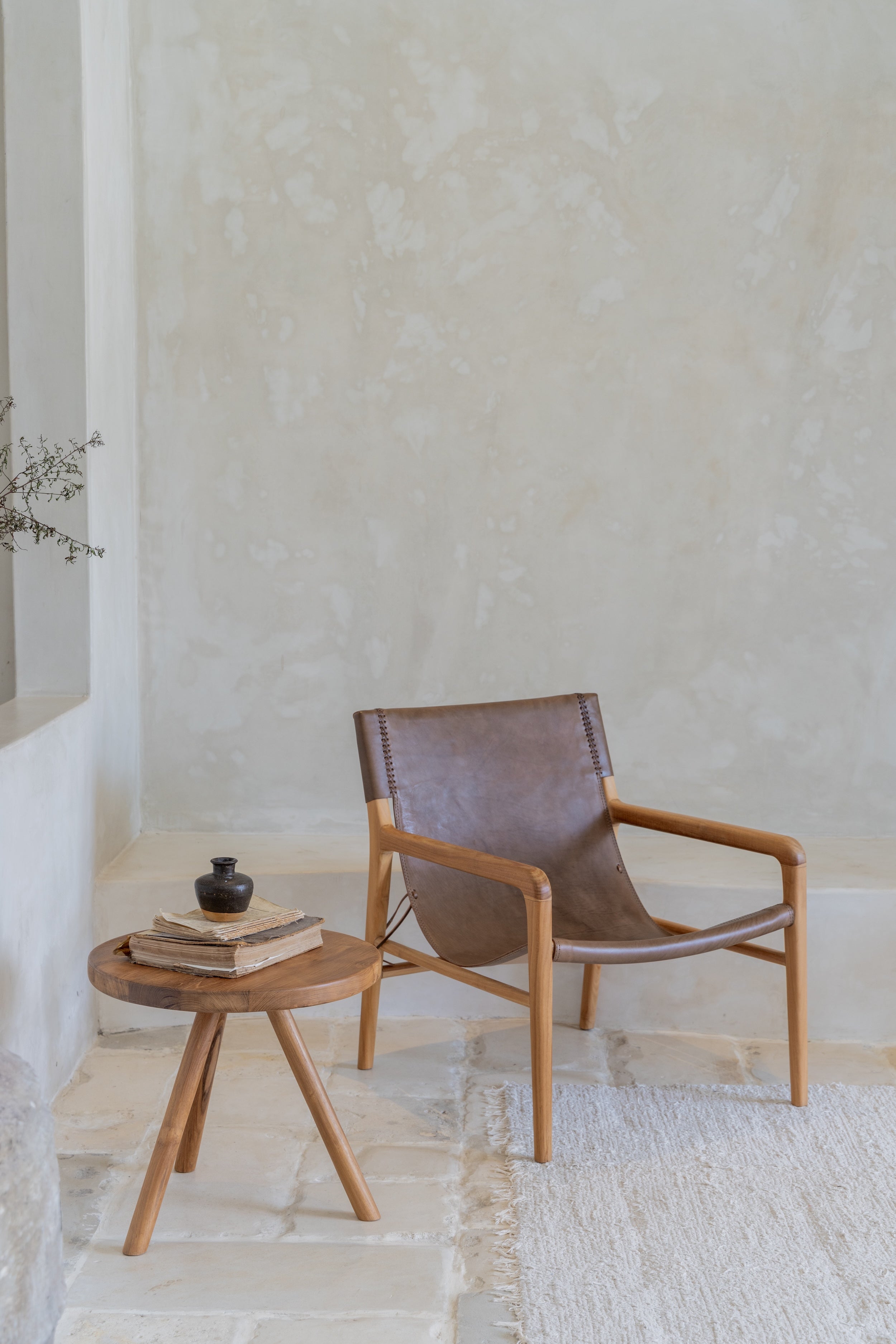 Fleur leather sling lounge chair in tan with continuous leather seat and back on recycled teak frame, in setting with side table